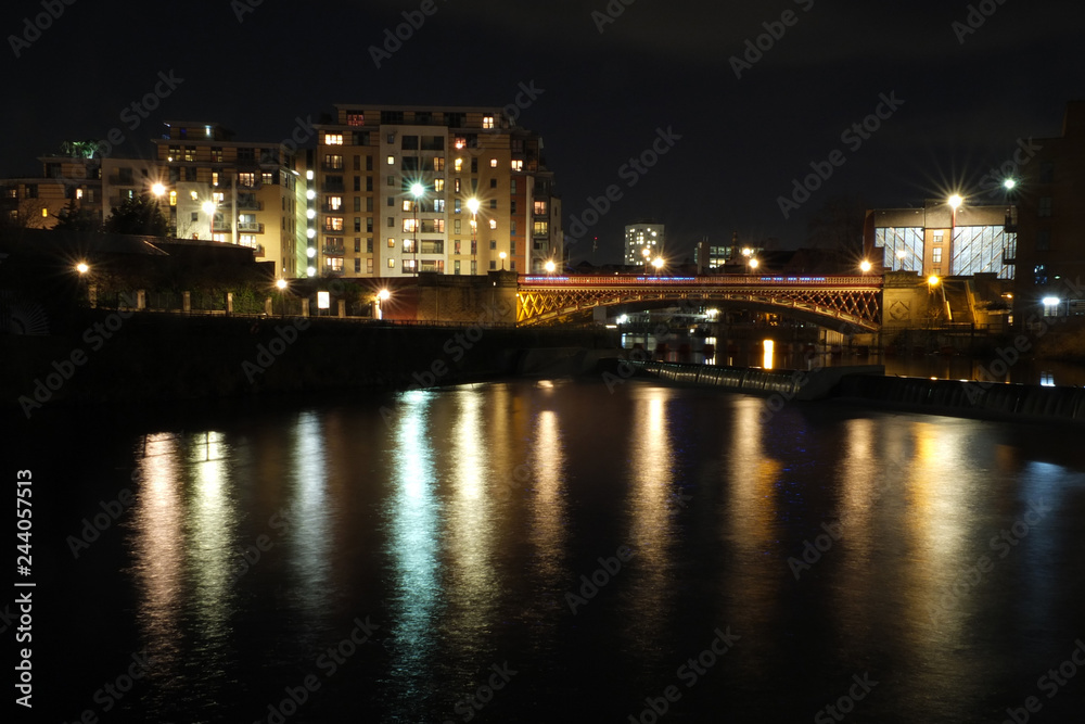 the river aire in leeds at night showing buildings on both sides of crown point bridge and the weir