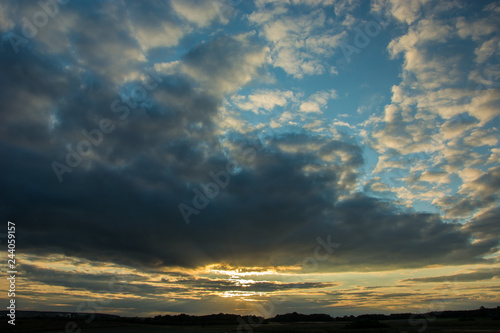 Canvas Print Sunset piercing through gray evening clouds in the blue sky
