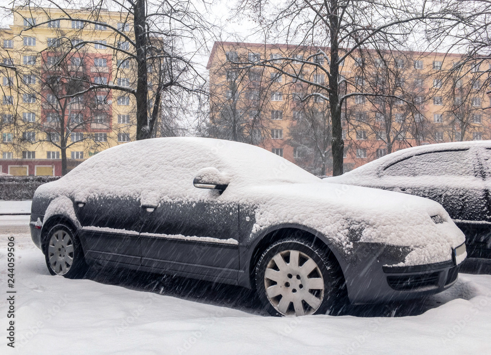 Grey sedan car covered by snow in a winter snowstorm