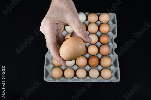 Man holding one egg in his hand, taken from a cardboard egg box on black mat background