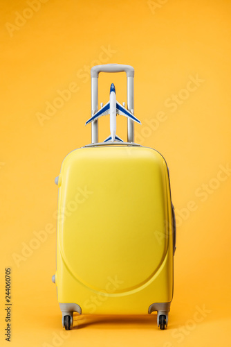 travel bag with wheels and toy plane on yellow background