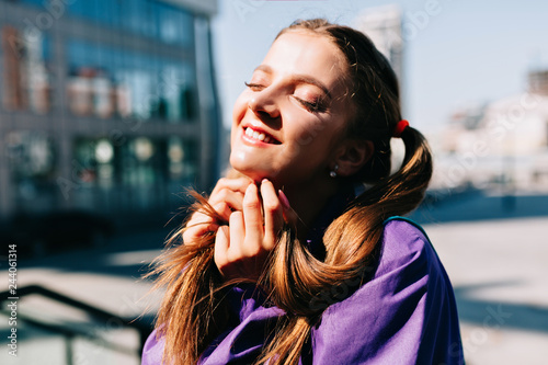 ?alm amazing woman with closed eyes enjoying a walking in sunlight in the city. Outdoor photo of good-humoured fashionable woman smiling in sunny good day