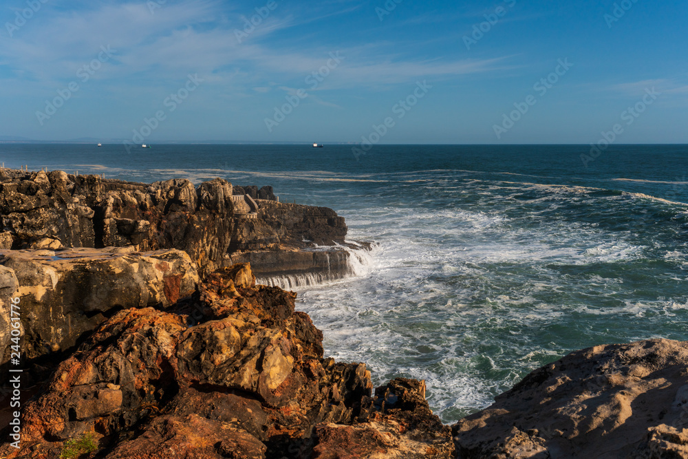 Stormy sea with waves breaking against the Portuguese eroded rocky coast. Rugged limestone coastline of Cascais, Portugal on a beautiful spring evening.