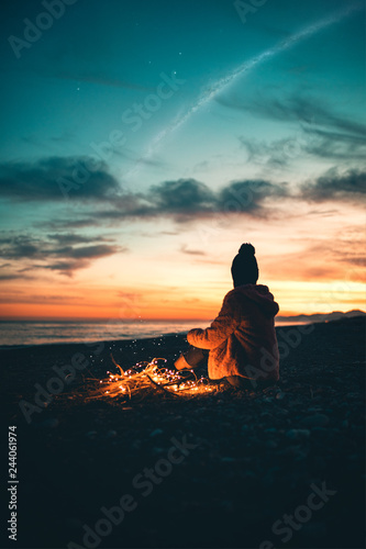 Una ragazza sola è seduta sulla spiaggia al tramonto a osservare il mare e il cielo rosso per rilassamento. photo