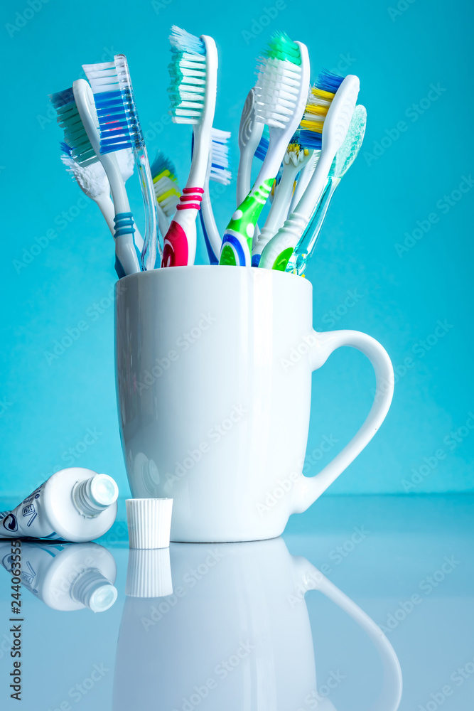 Multi-colored toothbrushes in a white mug close-up in the bathroom on a blue background.