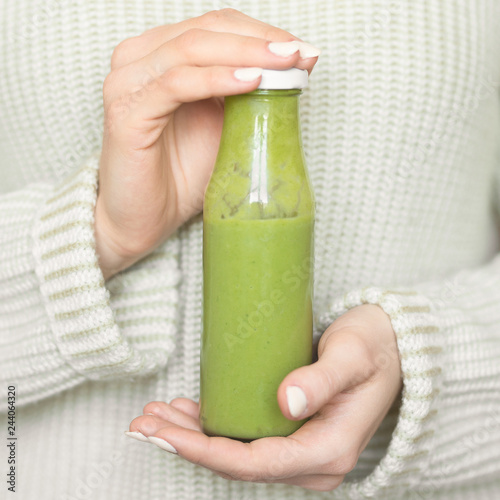 Winter seasonal smoothie drink detox. Girl in a woolen sweater, holding a bottle of green smoothie or juice. Diet, Clean Food, Weight Loss, Healthy Diet Concept