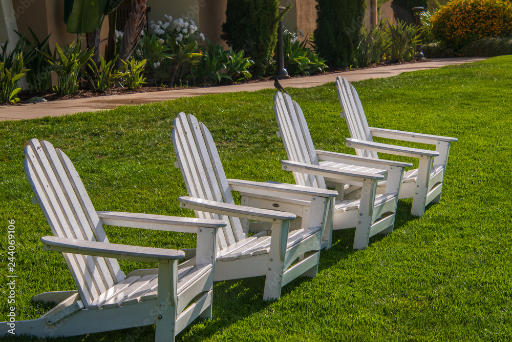 Group of four white Adirondack chairs on green lawn