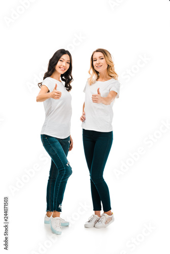 full length view of happy young women showing thumbs up and smiling at camera isolated on white