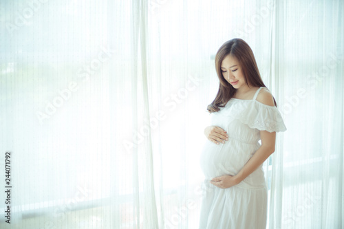 Free Download Young Asian beautiful pregnant woman standing near window - GFXLoad