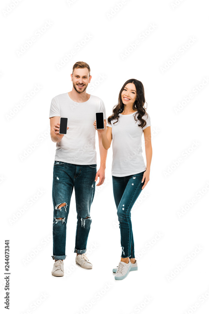 happy young couple holding smartphones with blank screens and smiling at camera isolated on white happy young couple holding smartphones with blank screens and smiling at camera isolated on white