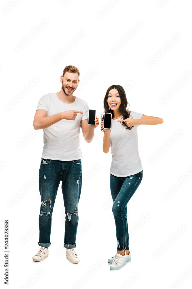 happy young couple pointing at smartphones with blank screens isolated on white happy young couple pointing at smartphones with blank screens isolated on white