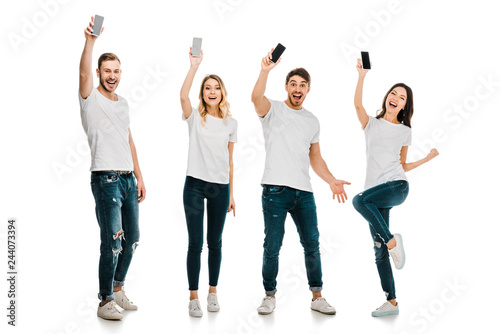 full length view of happy young men and women holding smartphones and smiling at camera isolated on white