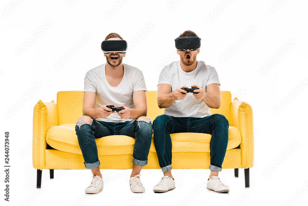 emotional young men in virtual reality headsets playing with joysticks isolated on white