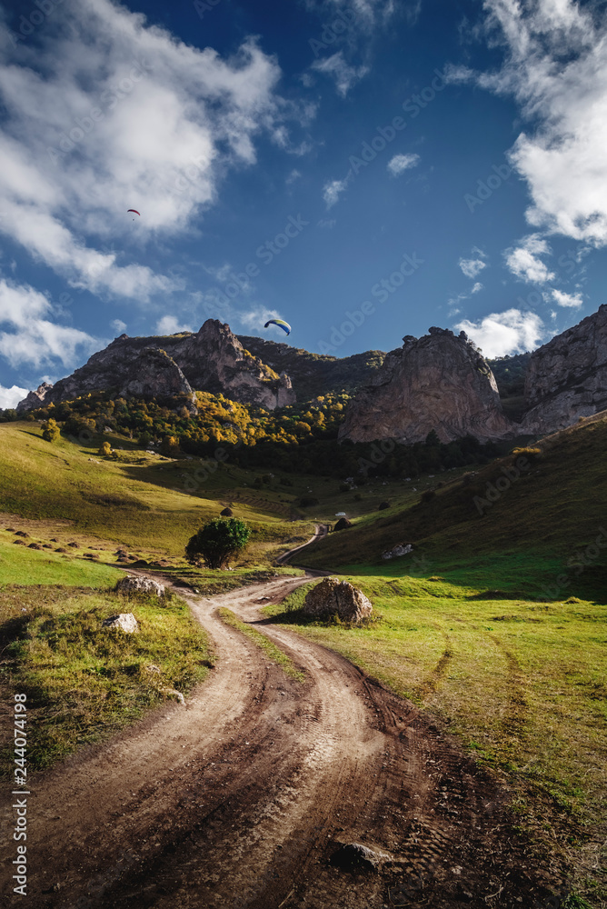 road in the field on the background of beautiful mountains and flying gliders road in the field on the background of beautiful mountains and flying gliders