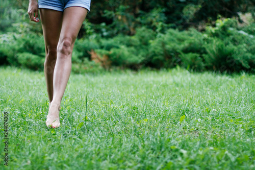 Female legs forward on green grass. Smooth skin