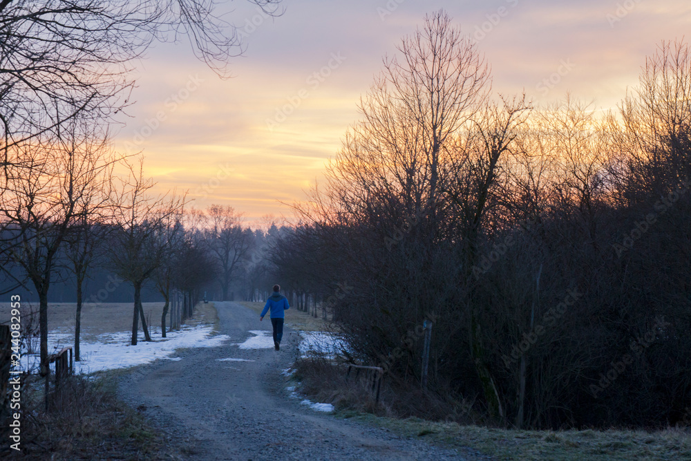 Jogger goes on a dirt road between trees in the direction of the rising sun which turns the sky red