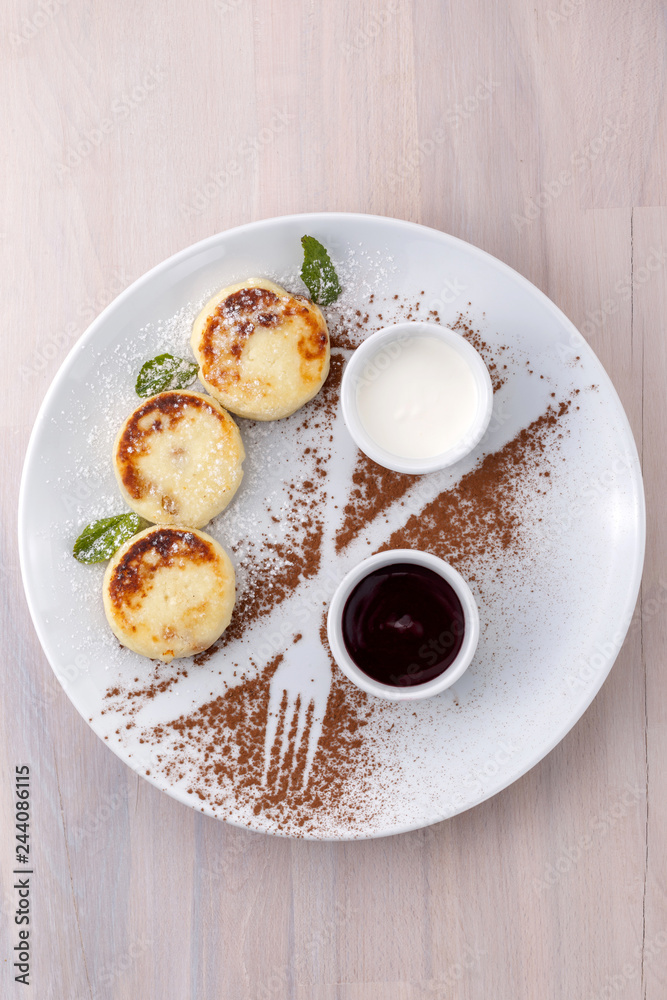 Cheese pancakes with currant jam and sour cream on a plate top view