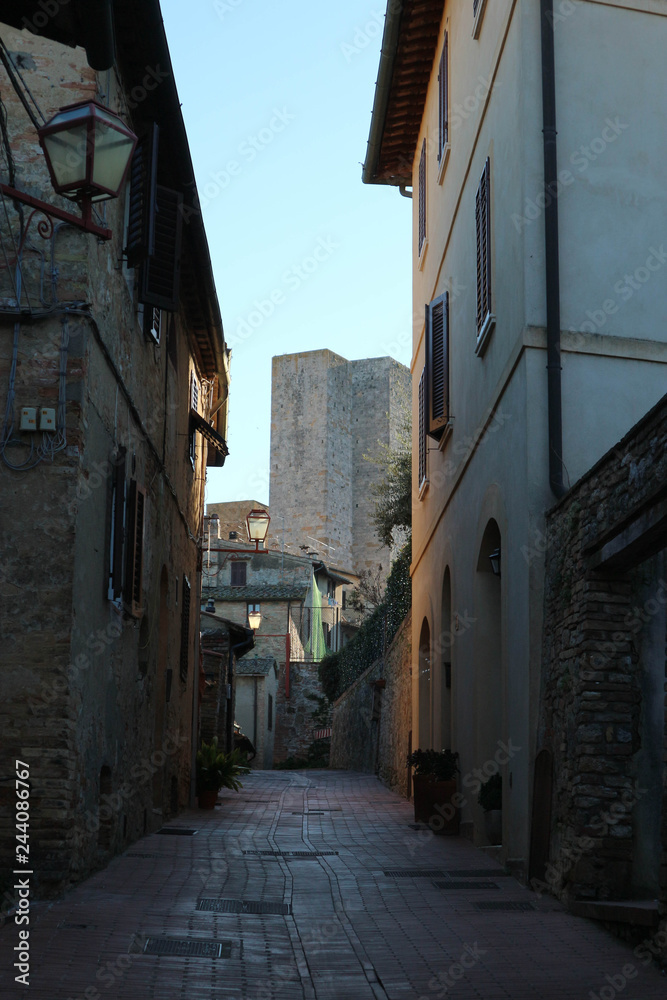 Medieval narrow street in old town San Gimignano with the famous towers at the background, Tuscany, Italy