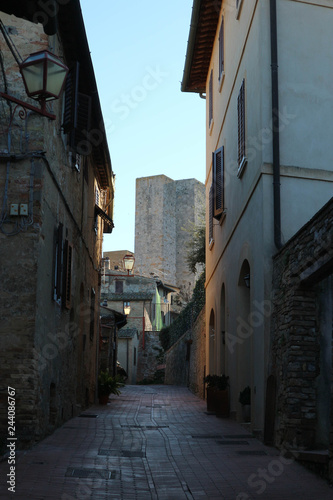 Medieval narrow street in old town San Gimignano with the famous towers at the background, Tuscany, Italy