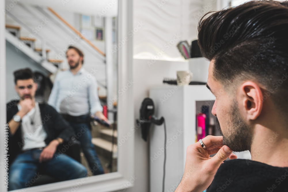 Fototapeta premium Handsome man at fashion stylist salon in front of mirror looking himself