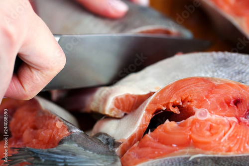 Hand with knife cuts fresh fish. Raw salmon carve steak