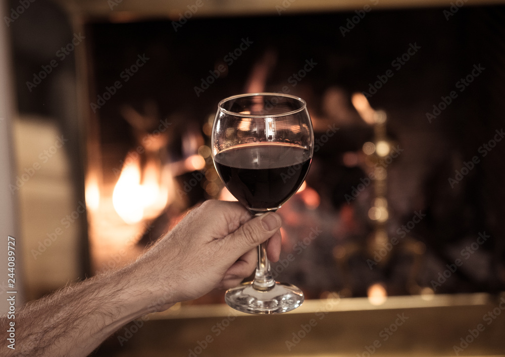Close up of happy man drinking wine relaxing by fire place at home in winter holidays vacation