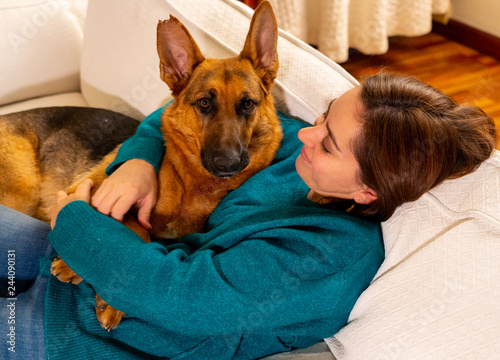 Cute portrait of young woman and dog german shepherd hugging at cozy home in winter