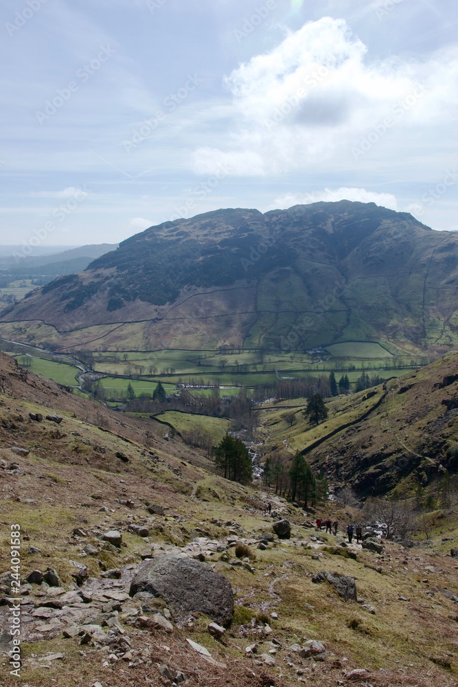 Rocky grass mountain moorland in foreground; pastoral fields below in mountain valley