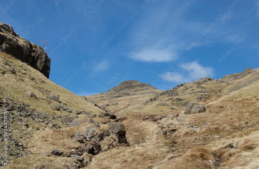 Marshy valley with mountain peaks, rocks, stream and footpath (Lake District) Marshy valley with mountain peaks, rocks, stream and footpath (Lake District)