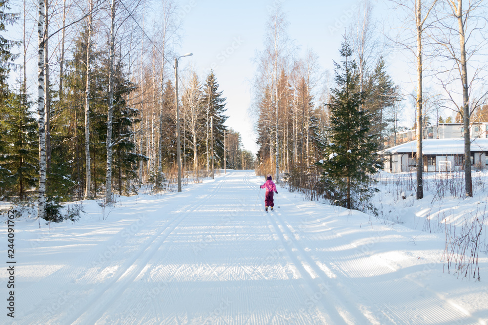 Fototapeta premium Small child in the ski track at winter forest in Finland.