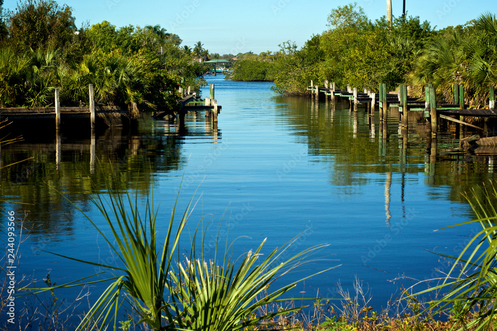 Looking out across the smooth clean water of canal, flanked with old boat docks and piers, in Bonita Springs, florida leading out to the gulf of mexico.