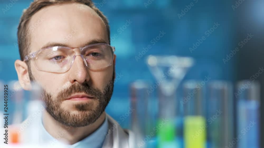 Close-up face of thoughtful male chemical worker looking on beaker with colorful liquid sample Close-up face of thoughtful male chemical worker looking on beaker with colorful liquid sample
