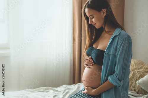 Attractive pregnant woman is sitting in bed and holding her belly. Last months of pregnancy. photo