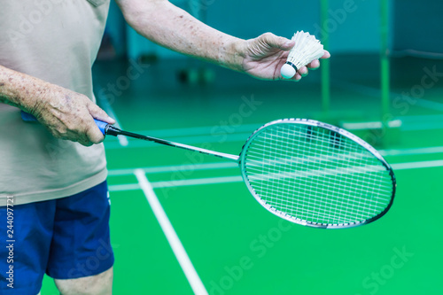 Male Senior Badminton single player hand holds white shuttle cock, ready to serve forehand with racket on green court. Sport, Game, Exercise, Competition, Practice, Training, Event and Health concept