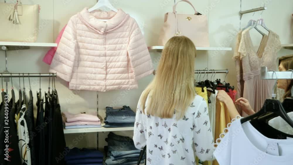Two happy young girls are choosing clothes in a department store. 4K Two happy young girls are choosing clothes in a department store. 4K