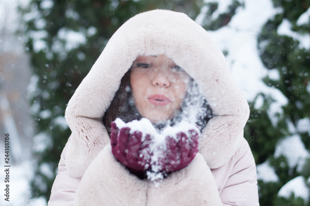 Portrait of young beautiful emotional woman in hooded down coat and gloves on snow covered garden background. Winter snowy landscape Portrait of young beautiful emotional woman in hooded down coat and gloves on snow covered garden background. Winter snowy landscape