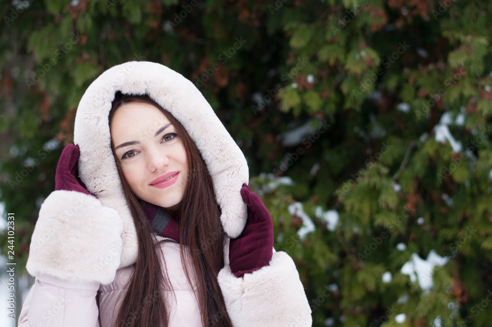 Portrait of young beautiful emotional woman in hooded down coat and gloves on snow covered garden background. Winter snowy landscape Portrait of young beautiful emotional woman in hooded down coat and gloves on snow covered garden background. Winter snowy landscape