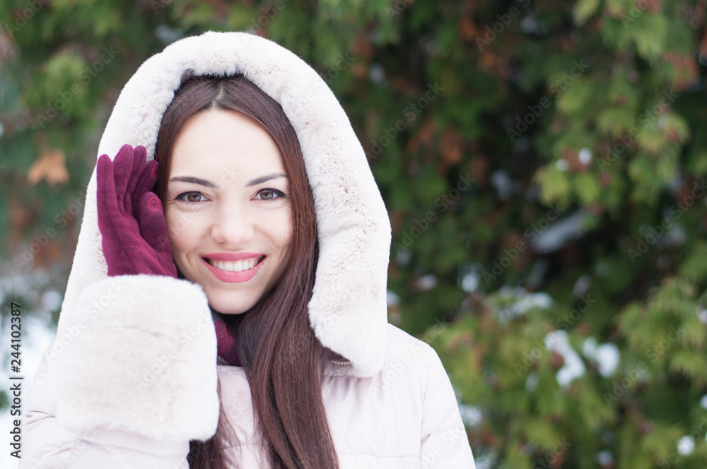 Portrait of young beautiful emotional woman in hooded down coat and gloves on snow covered garden background. Winter snowy landscape Portrait of young beautiful emotional woman in hooded down coat and gloves on snow covered garden background. Winter snowy landscape