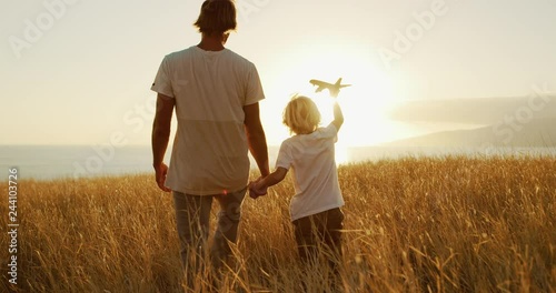 Adorable father and son walking together through golden field at sunset