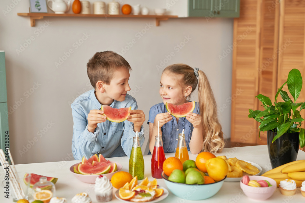 Children eat fruit pineapple, watermelon, apples and drink drinks with chia. Healthy food in the children's menu. Happy children with fruits and fresh juice in kitchen, kids healthy eating concept Children eat fruit pineapple, watermelon, apples and drink drinks with chia. Healthy food in the children's menu. Happy children with fruits and fresh juice in kitchen, kids healthy eating concept