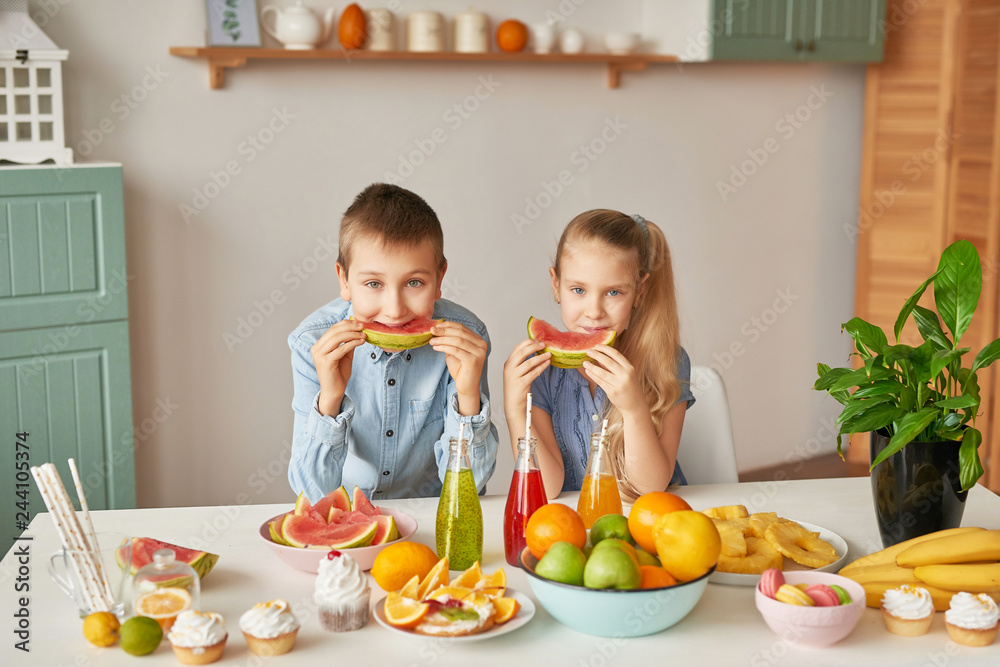Children eat fruit pineapple, watermelon, apples and drink drinks with chia. Healthy food in the children's menu. Happy children with fruits and fresh juice in kitchen, kids healthy eating concept Children eat fruit pineapple, watermelon, apples and drink drinks with chia. Healthy food in the children's menu. Happy children with fruits and fresh juice in kitchen, kids healthy eating concept