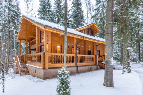 Fotografering Snow-covered beautiful wooden house in the forest at dusk