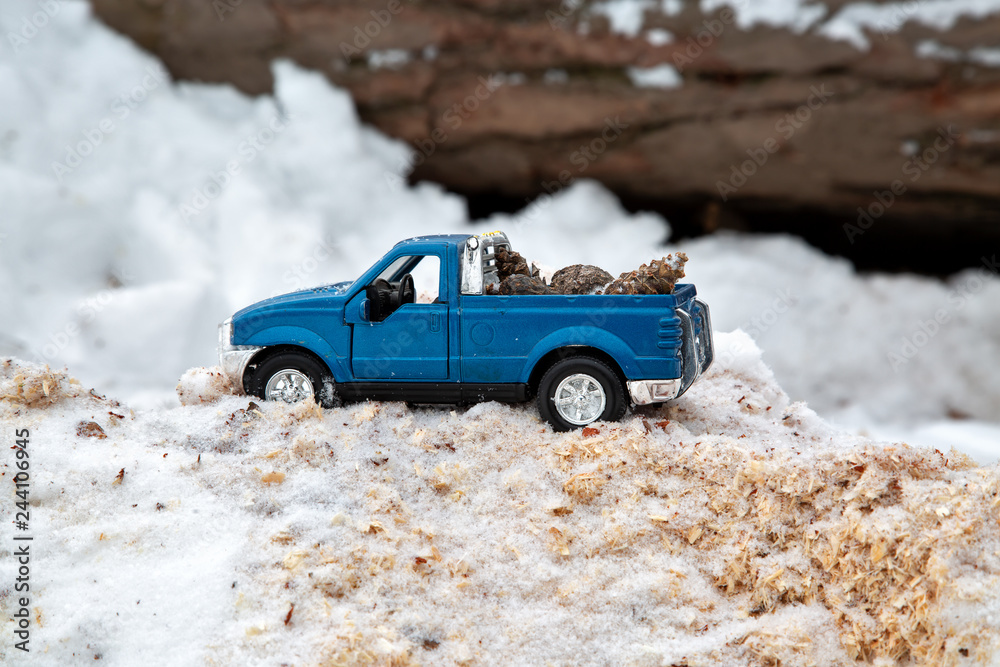 Obraz premium Blue toy pickup truck in sawmill. Stuck at snowdrift and sawdust. Carrying fir cones in the back of a car body.