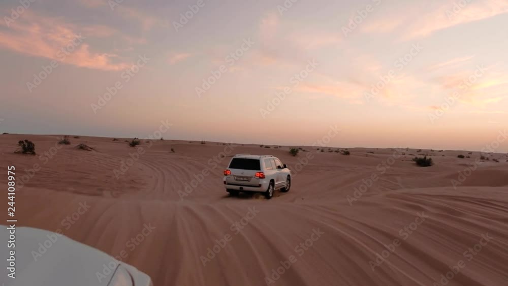 view out off moving car cabin window on forward luxury jeeps driving among fantastic desert tracks at sunset view out off moving car cabin window on forward luxury jeeps driving among fantastic desert tracks at sunset