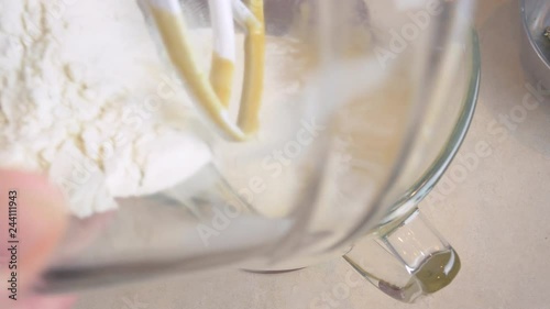 Pouring flour into a red stand mixer and mixing cookie batter in 4k. A woman dumps ingredients from a glass bowl into the electric kitchen appliance and turns the paddle on. Top view for gif recipes.