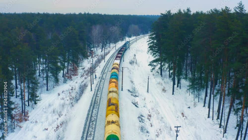 Aerial following view of the freight train, carrying tank cars with oil and cargo containers, moving on the winter snowy forest Aerial following view of the freight train, carrying tank cars with oil and cargo containers, moving on the winter snowy forest