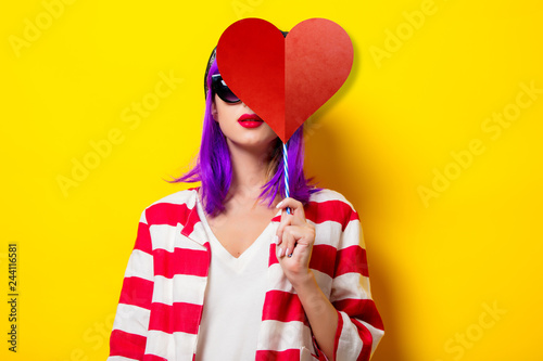 Young girl with purple hair holding heart shape on yellow background