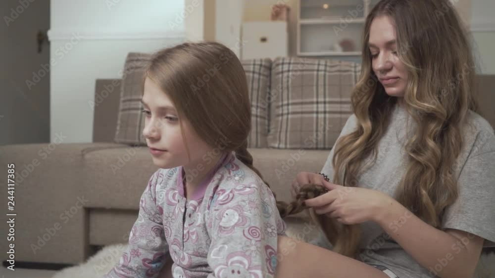 Older sister combing hair of younger girl sitting on fluffy carpet on the floor near couch at home. Sisters relationship Older sister combing hair of younger girl sitting on fluffy carpet on the floor near couch at home. Sisters relationship