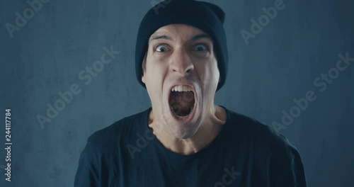 Portrait of angry hipster man in black cap screaming with agression. Threat of violence.