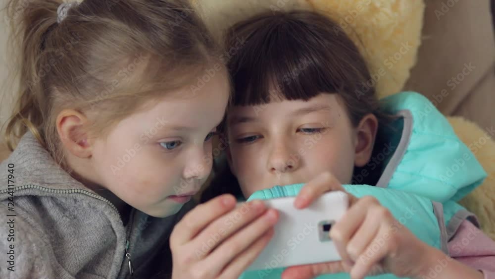 children play online games, two sisters with a smartphone in their hands children play online games, two sisters with a smartphone in their hands